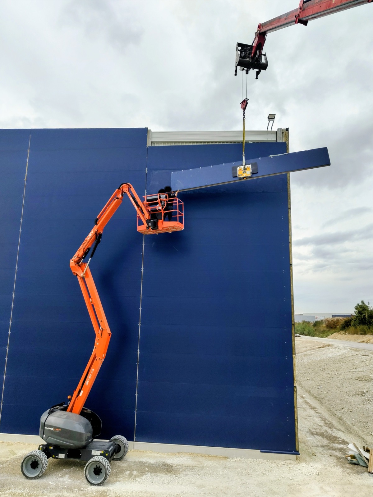 Palonnier à ventouses posant panneau bardage bleu en façade — MTLOC